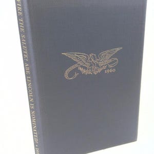 May include: A navy blue book with gold lettering and an emblem featuring an eagle. The book's spine reads "FIRE THE SALUTE! ABE LINCOLN IS NOMINATED! - 1860." The cover displays "CENTENNIAL EDITION 1960".
