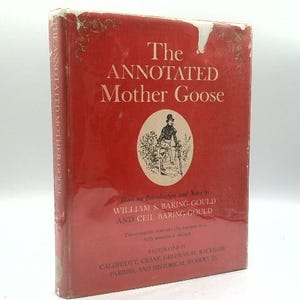 May include: A red hardcover book titled The Annotated Mother Goose by William S. Baring-Gould and Ceil Baring-Gould. The front cover features a central circular illustration of a person in a top hat and includes text listing various illustrators.