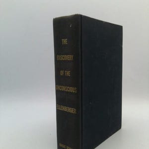 May include: A black hardcover book titled The Discovery of the Unconscious by Ellenberger, published by Basic Books. The spine features gold lettering that clearly displays the title, author name, and publisher at the bottom of the book.