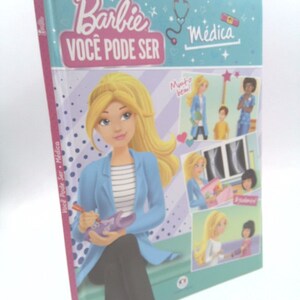 May include: A pink and blue book with the title "Barbie Você Pode Ser Médica" and an illustration of Barbie dressed as a doctor. The book features several images of Barbie in different medical scenarios.