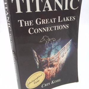 May include: A black hardcover book titled "Titanic: The Great Lakes Connections" by Cris Kohl. The book cover features a photo of the Titanic wreck and a map of the Great Lakes. The book is signed "Autographed Copy".