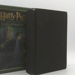 May include: A hardcover book titled "Harry Potter and the Half-Blood Prince" with a dark green cover and a black spine. The cover features an illustration of Harry Potter and Dumbledore. The book is in good condition.