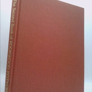 May include: A red book with the title "The Second Book of Rookwood Pottery" by Herbert Peck.