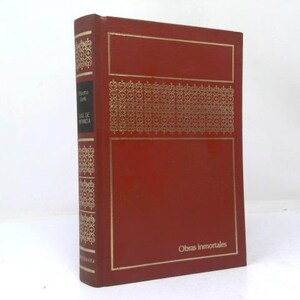 May include: A red hardcover book with gold foil detailing on the front cover and spine. The front cover features a decorative geometric pattern and the text Obras Inmortales. The spine includes the text Emma and Luz de Infancia in white.