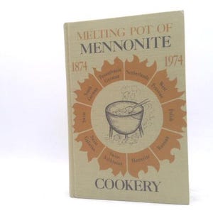 May include: A vintage cookbook titled "Melting Pot of Mennonite Cookery" with a beige cover. The cover features a central illustration of a pot with steam, surrounded by text and dates 1874 and 1974. The book's title and the word "Cookery" are also visible.