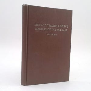 May include: A brown hardcover book titled Life and Teaching of the Masters of the Far East Volume II. The front cover features silver embossed text centered on the solid brown surface. The book is positioned upright, showing the front cover and spine.