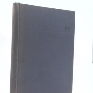 May include: A navy blue hardcover book with a rectangular shape. The book has a horizontal line across the center and a small emblem in the upper right corner. The spine is dark and the pages are not visible.