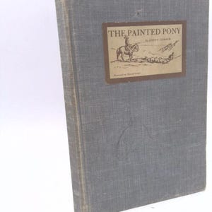 May include: A vintage hardcover book with a blue cloth cover. The title "THE PAINTED PONY" by John C. Almack is printed on the front cover with an illustration of a cowboy riding a horse.