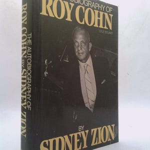 May include: A hardcover book titled "The Autobiography of Roy Cohn" by Sidney Zion. The book has a black cover with gold lettering and a portrait of Roy Cohn. The spine also features the title and author's name.