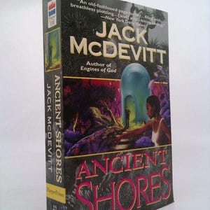 May include: A hardcover book titled "Ancient Shores" by Jack McDevitt. The cover features a vibrant illustration with a woman reaching towards a figure in a doorway. The author's name and book title are prominently displayed in white and red.