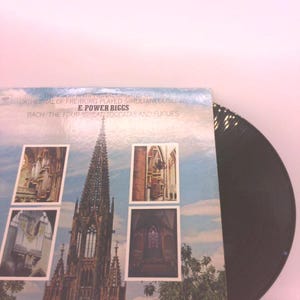 May include: A vinyl record with a cover featuring a cathedral and the text "THEISOR ANTIPHONAL ONEINS OF THE CATHEDRAL OF FREIBURG PLAYED SIMULTANEOUSLY BY E. POWER BIGGS BACH/THE FOUR GREAT TOCCATAS AND FUGUES". The record is black.