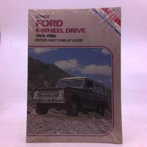 May include: A vintage repair and tune-up guide for Ford 4-wheel drive vehicles from 1969-1986. The cover features a dark-colored SUV on a rocky terrain under a cloudy sky. The book is sealed in plastic.