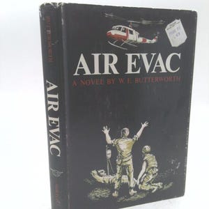 May include: A hardcover book titled "AIR EVAC" by W.E. Butterworth. The cover is black with an illustration of a helicopter and figures. The spine reads "AIR EVAC" and "BUTTERWORTH". A price tag is visible.