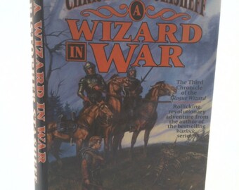 May include: A Wizard in War book cover featuring a fantasy illustration of a group of people on horseback riding through a forest. The book is the third in the Rogue Wizard series.