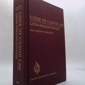 May include: A burgundy-colored book titled "Code of Canon Law, Latin-English Edition." The book's spine and cover feature gold lettering. The Canon Law Society of America logo is visible. The book is a new English translation.