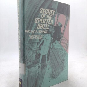 May include: A vintage hardcover book titled "Secret of the Spotted Shell" by Phyllis A. Whitney, illustrated by John Mecray. The cover features a teal background with a drawing of a girl and a man on a bridge. The book's spine is also teal.