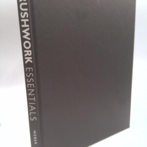 May include: A hardcover book titled "BRUSHWORK ESSENTIALS" by Weber. The book has a dark gray cover and the title is printed vertically in white. The book is standing upright against a white background.