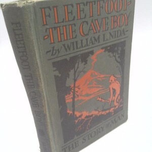 May include: A vintage book titled "Fleetfoot the Cave Boy" by William L. Nida. The cover is a muted green with orange lettering and a graphic illustration of a caveman and a mountain scene. The book's spine also displays the title.