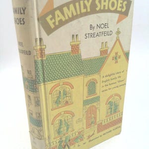 May include: A vintage hardcover book titled "Family Shoes" by Noel Streatfeild. The cover features an illustration of a yellow house with green roof tiles and a brown chimney. The book is illustrated by Richard Floethe.