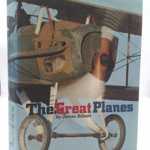 May include: The cover of a book titled "The Great Planes" by James Gilbert. The cover features a close-up of a vintage biplane with a propeller and wheels.