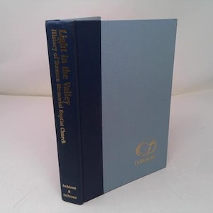 May include: A hardcover book titled "Light in the Valley, History of Dawson Memorial Baptist Church." The spine is dark blue with gold lettering. The cover is light blue with a gold logo and the word "DENISON".
