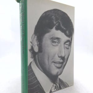 May include: A hardcover book with a black and white portrait of a man on the cover. The man is wearing a suit and tie. The spine is green with white text.