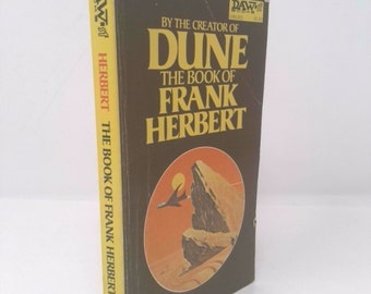 May include: A brown paperback book with a yellow spine. The cover features a desert landscape with a flying vehicle and the text "By the creator of Dune The Book of Frank Herbert".