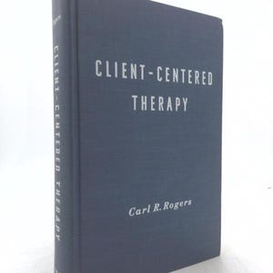 May include: A hardcover book titled "CLIENT-CENTERED THERAPY" by Carl R. Rogers. The book has a dark blue cover with white lettering. The title is centered on the front, and the author's name is at the bottom.
