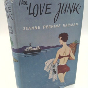 May include: The cover of a vintage paperback book titled "The 'Love Junk'" by Jeanne Perkins Harman. The cover features a woman in a red and white swimsuit standing in the water with a towel in her hand. A boat is in the background.