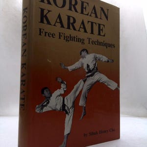 May include: A hardcover book titled Korean Karate Free Fighting Techniques by Sihak Henry Cho. The cover features a brown and orange gradient background with black text and a black and white photograph of two individuals in white karate uniforms.
