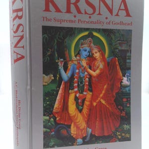 May include: A book titled "Krsna: The Supreme Personality of Godhead" by A.C. Bhaktivedanta Swami Prabhupada. The cover features a colorful illustration of Krishna and Radha in a garden setting.