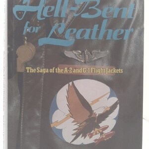 May include: A book titled "Hell-Bent for Leather: The Saga of the A-2 and G-1 Flight Jackets" by Derek Nelson and Dave Parsons. The cover features a brown leather jacket with a winged insignia and a patch depicting an eagle with a lightning bolt and bombs.