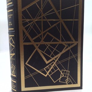 May include: A hardcover book with a black cover and gold geometric design. The spine features the title "Motherly Love" and "Signed First Edition" in gold lettering. The book is part of "The Franklin Library" series.