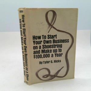 May include: A hardcover book with a beige dust jacket featuring a brown shoestring graphic. The title reads How To Start Your Own Business on a Shoestring and Make up to $100,000 a Year by Tyler G. Hicks. The text is printed in black ink.