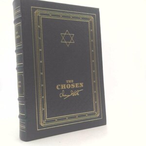 May include: A hardcover book titled "The Chosen" with gold lettering and a Star of David on the cover. The book has a dark cover with gold decorative borders and spine details.