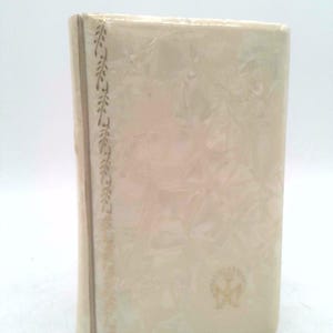 May include: A white book with a gold embossed design on the cover. The book has a gold border with a floral pattern. The book has a gold logo on the bottom right corner.