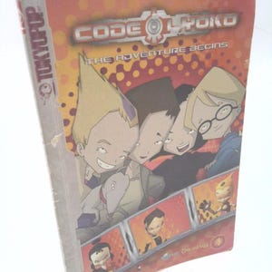 May include: A paperback book titled "Code Lyoko: The Adventure Begins" with a cover featuring cartoon characters. The cover is predominantly orange and red with the Tokyopop logo on the spine. The book is slightly angled.