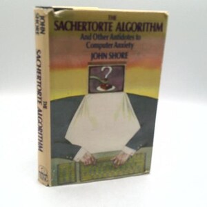 May include: A hardcover book titled The Sachertorte Algorithm and Other Antidotes to Computer Anxiety by John Shore. The cover features a surreal illustration of a person in a suit with a computer monitor for a head, displaying a question mark.