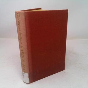 May include: A hardcover book titled "The Care and Feeding of Garden Plants." The book has a reddish-brown cover and a light tan spine with gold lettering. The book is standing upright.