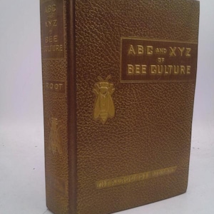 May include: A vintage book titled "ABC and XYZ of Bee Culture" with embossed text and a bee emblem. The cover is a textured brown with gold lettering. The book's spine also features text and is a darker brown.