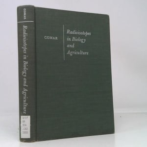 May include: A hardcover book titled "Radioisotopes in Biology and Agriculture" by COMAR. The book has a dark green cover with white text. The spine displays the title and publisher. The book is standing upright.