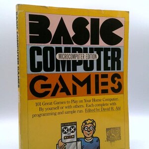 May include: A yellow paperback book titled BASIC COMPUTER GAMES Microcomputer Edition, edited by David H. Ahl. The cover features bold black text, a subtitle about 101 games, and a cartoon illustration of a person standing next to a robot.