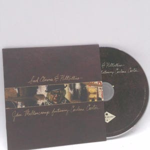 May include: A CD album titled "Sad Clowns & Hillbillies" featuring John Mellencamp and Carlene Carter. The album cover is brown with a photo of a person wearing a hat. The CD is visible next to the album cover.