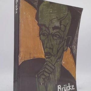 May include: A book with a painting of a person's face in green and black. The person is depicted with a pensive expression, with their hand near their chin. The word "Brücke" is printed in white on the cover.