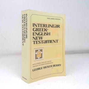 May include: A light yellow hardcover book titled Interlinear Greek-English New Testament, King James Version, by George Ricker Berry. The cover features dark brown text and a small square graphic of a cross. The spine also displays the title.