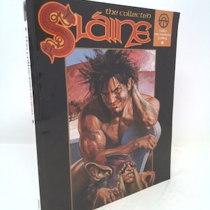 May include: A black hardcover book with a red and gold illustration of a warrior on the cover. The title "The Collected Slaine" is written in red and gold lettering. The book is part of the "Mills & Boon Collector's Library" series.