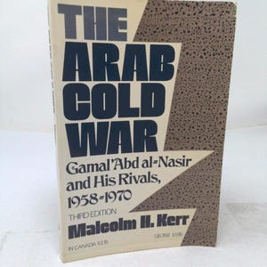 May include: A paperback book titled The Arab Cold War: Gamal 'Abd al-Nasir and His Rivals, 1958-1970, Third Edition by Malcolm H. Kerr. The cover features bold dark blue text on a cream background with a brown speckled lightning bolt graphic.