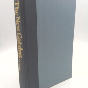 May include: A hardcover book titled "The New Gatsbys" by Bob Tananbaum. The book has a dark gray spine with gold lettering and a light gray cover. The publisher's name, Morrow, is at the bottom of the spine.