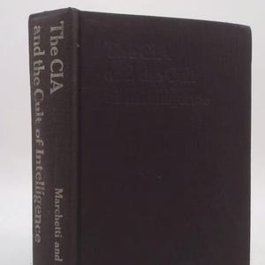 May include: A black hardcover book titled The CIA and the Cult of Intelligence by Marchetti and Marks. The title and author names are printed in white on the spine. The front cover features the same title in a subtle, embossed black finish.