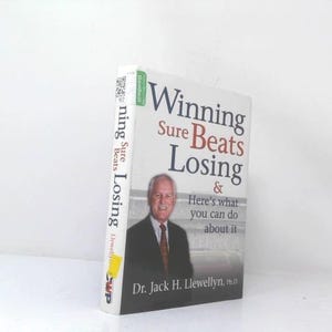 May include: A hardcover book titled Winning Sure Beats Losing & Here's what you can do about it by Dr. Jack H. Llewellyn, Ph.D. The cover features a photograph of a man in a suit and tie against a gray background with text in black and red.
